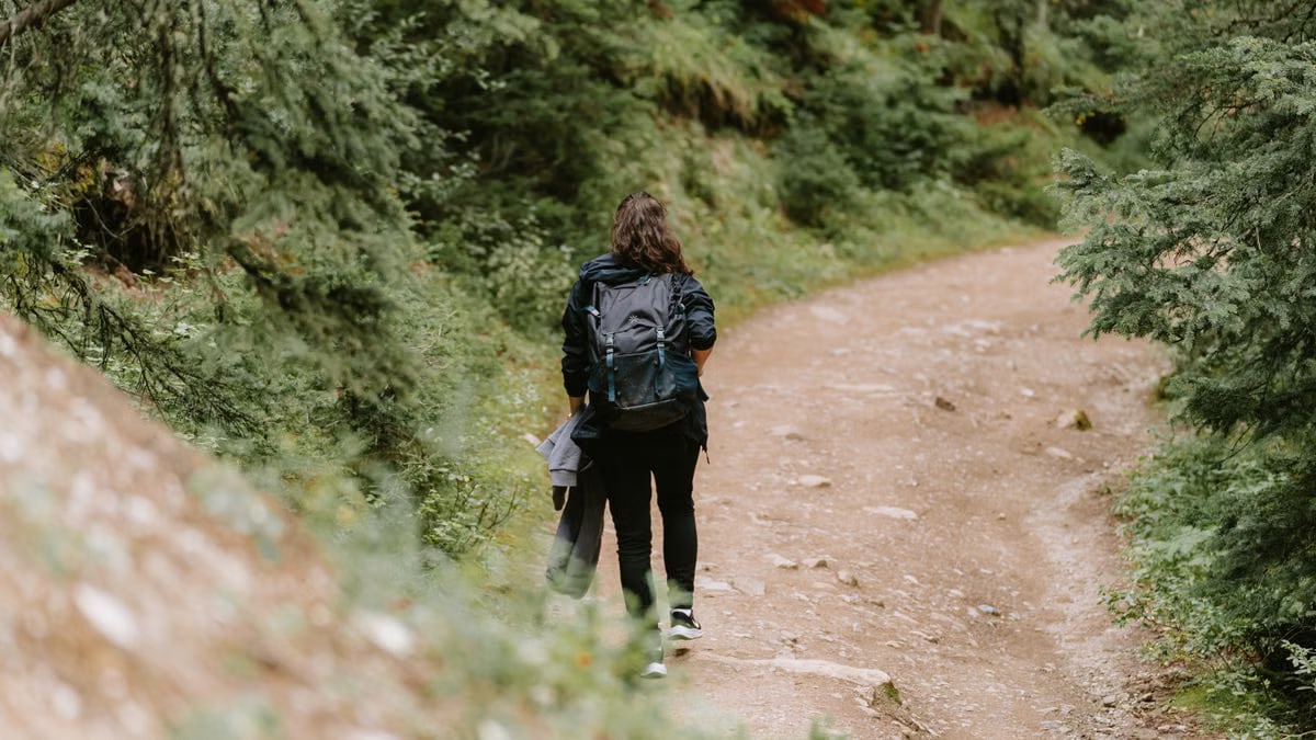 A woman hiking with a backpack on a scenic dirt road in Banff, surrounded by lush trees.